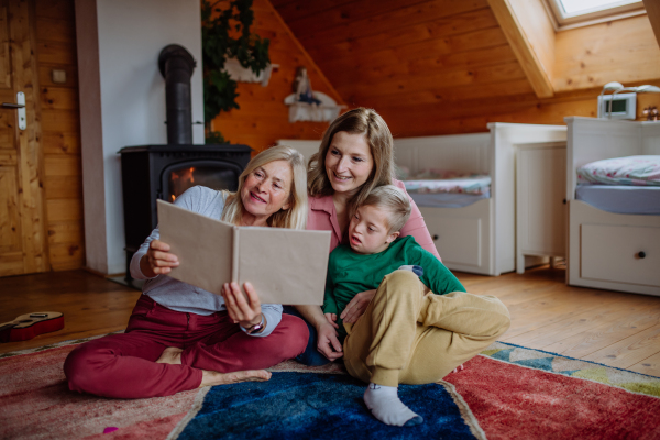 A boy with Down syndrome with his mother and grandmother looking at family photo album at home.