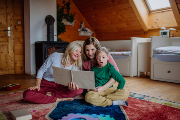 A boy with Down syndrome with his mother and grandmother looking at family photo album at home.