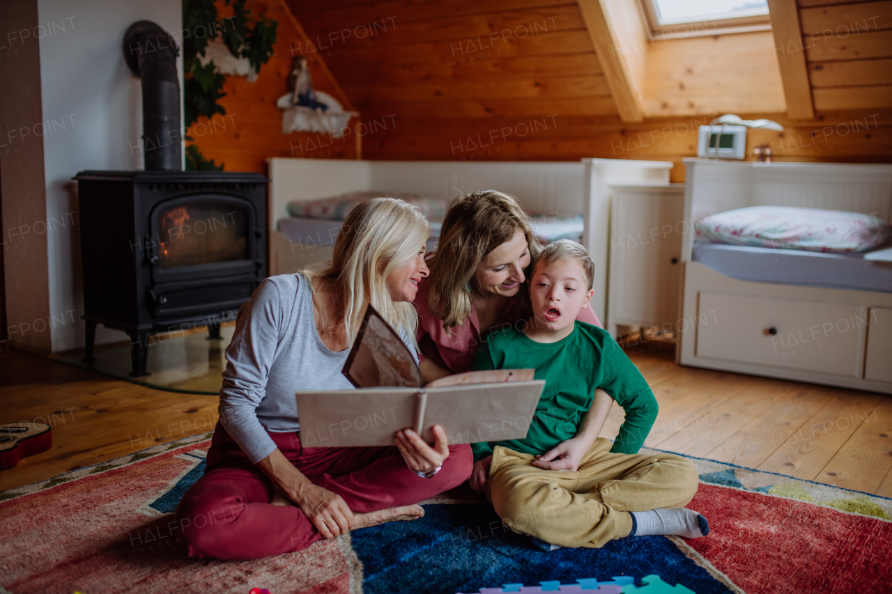 A boy with Down syndrome with his mother and grandmother looking at family photo album at home.