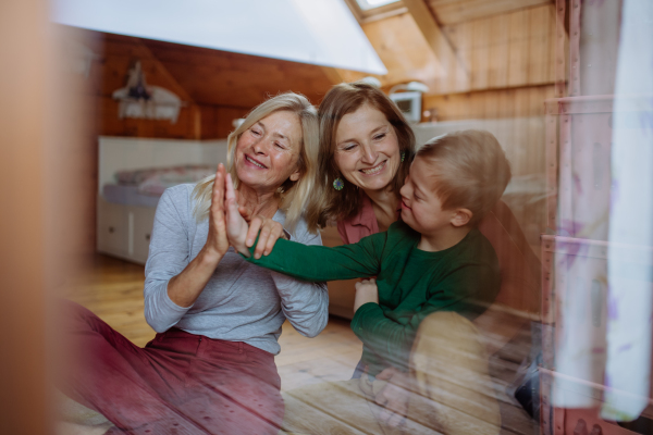 A boy with Down syndrome with his mother and grandmother sitting and looking through window at home.