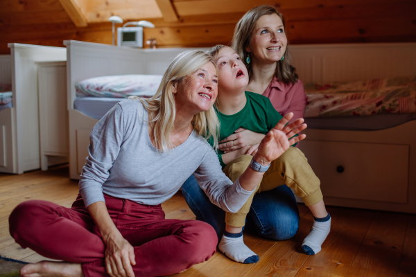 A boy with Down syndrome with his mother and grandmother sitting and looking up. at home.