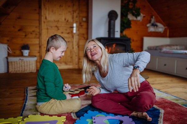 A boy with Down syndrome sitting on floor and playing with his grandmother at home