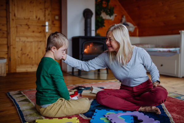 A boy with Down syndrome sitting on floor and playing with his grandmother at home