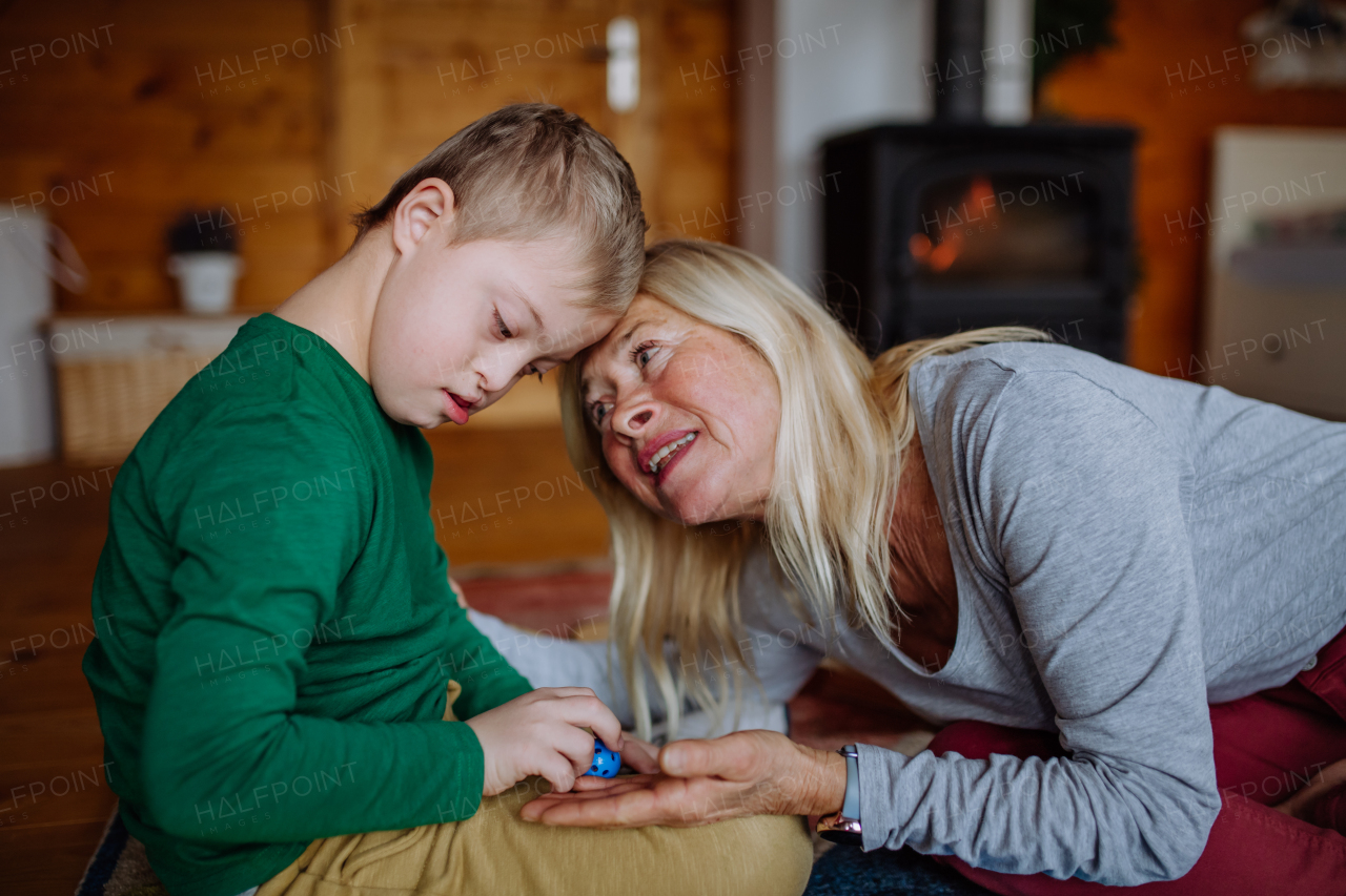 A boy with Down syndrome sitting on floor and playing with his grandmother at home