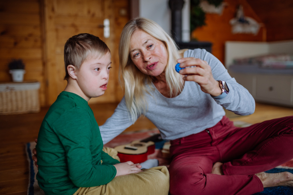 A boy with Down syndrome sitting on floor and playing with his grandmother at home