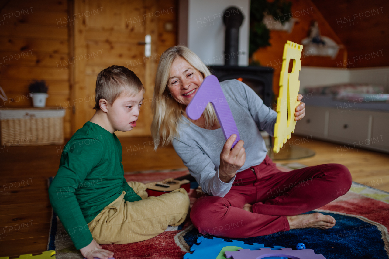 A boy with Down syndrome sitting on floor and playing with his grandmother at home