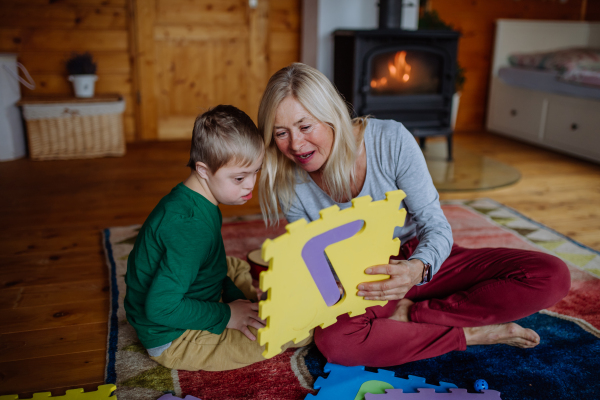 A boy with Down syndrome sitting on floor and playing with his grandmother at home