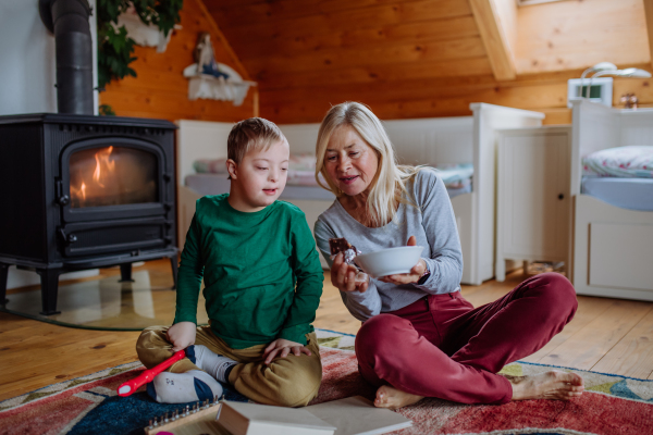 A boy with Down syndrome sitting on floor and playing with his grandmother at home