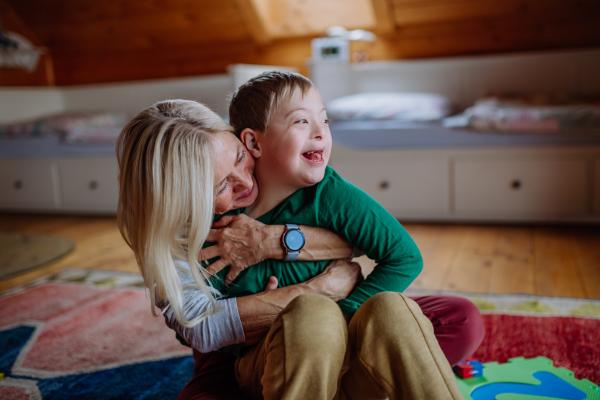 A happy boy with Down syndrome sitting on floor and hugging with his grandmother at home