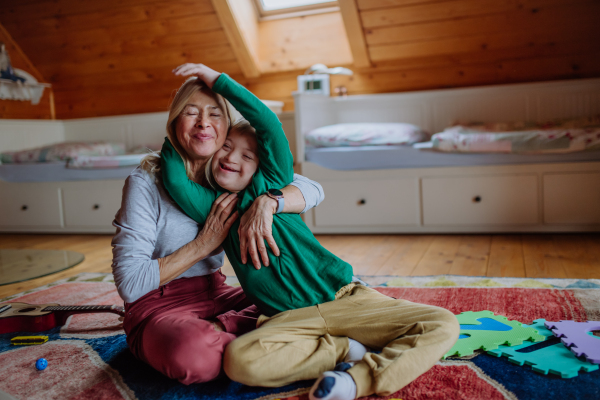 A happy boy with Down syndrome sitting on floor and hugging with his grandmother at home