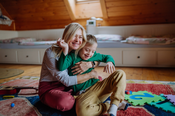 A happy boy with Down syndrome sitting on floor and hugging with his grandmother at home