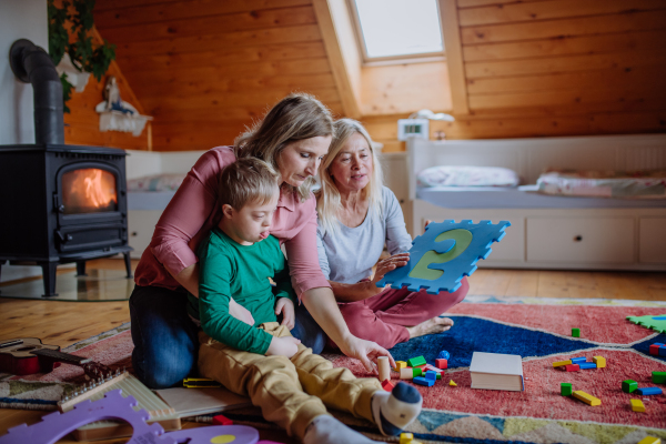 A boy with Down syndrome sitting on floor and playing with his mother and grandmother at home