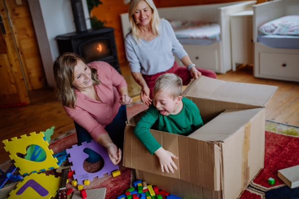 A boy with Down syndrome with his mother and grandmother playing with box together at home.