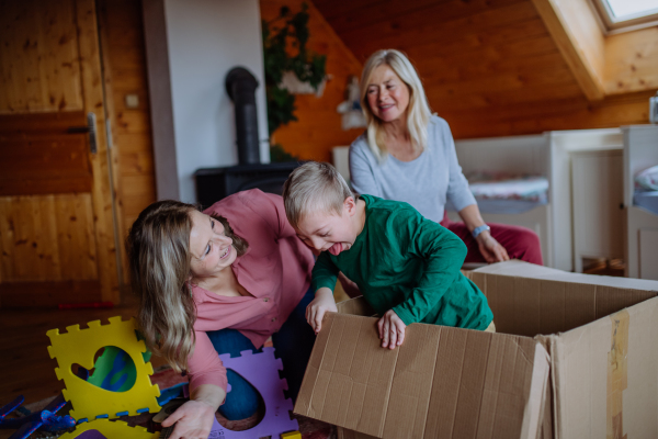 A boy with Down syndrome with his mother and grandmother playing with box together at home.