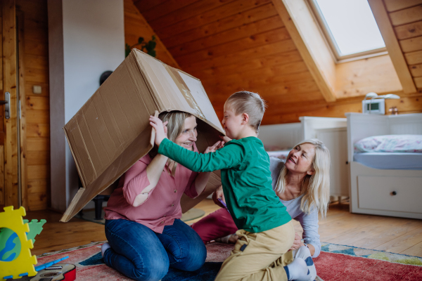 A boy with Down syndrome with his mother and grandmother playing with box together at home.