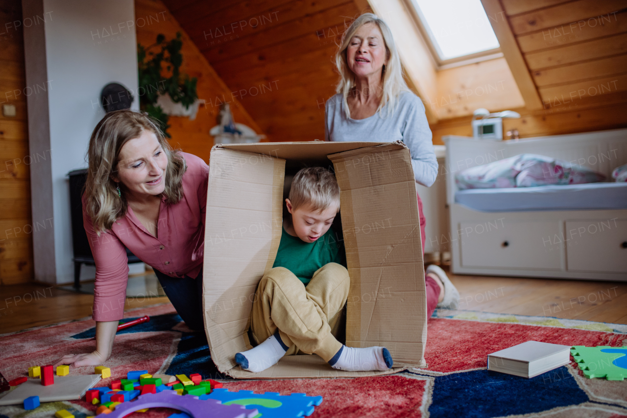 A boy with Down syndrome with his mother and grandmother playing with box together at home.