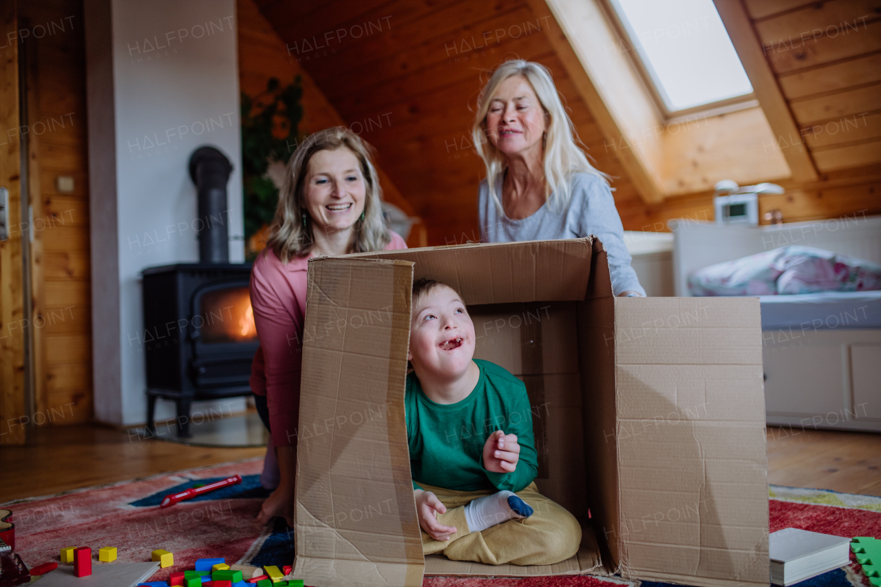 A boy with Down syndrome with his mother and grandmother playing with box together at home.