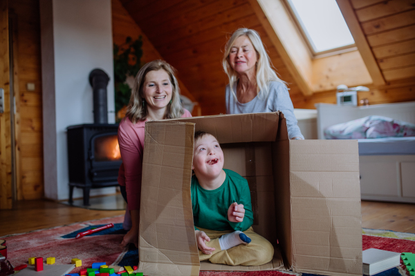 A boy with Down syndrome with his mother and grandmother playing with box together at home.