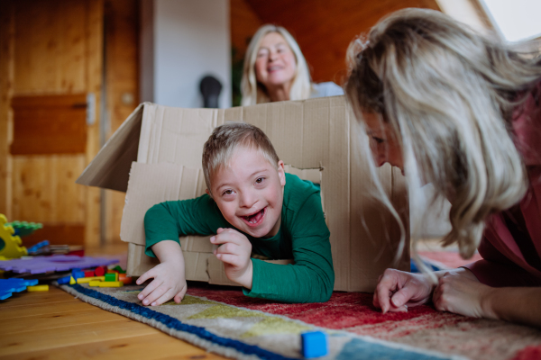 A boy with Down syndrome with his mother and grandmother playing with box together at home.