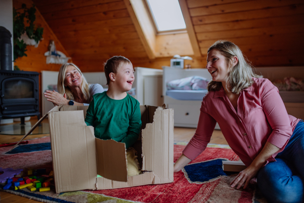 A boy with Down syndrome with his mother and grandmother playing with box together at home.