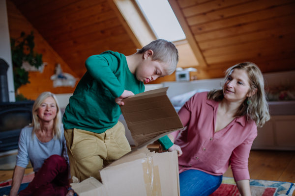 A boy with Down syndrome with his mother and grandmother playing with box together at home.