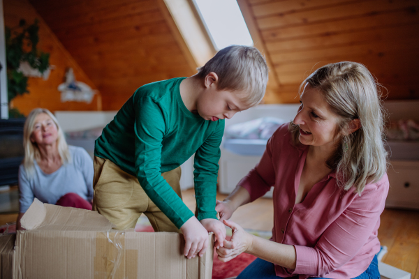 A boy with Down syndrome with his mother and grandmother playing with box together at home.