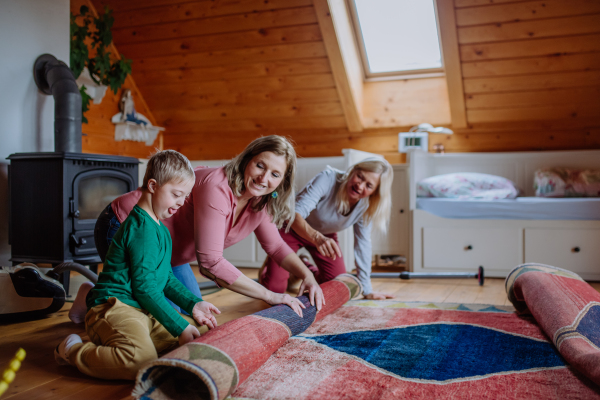 A boy with Down syndrome with his mother and grandmother rolling up the carpet at home.