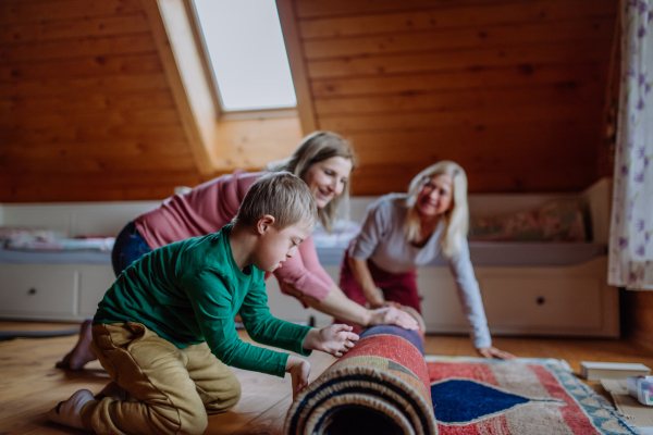 A boy with Down syndrome with his mother and grandmother rolling up the carpet at home.