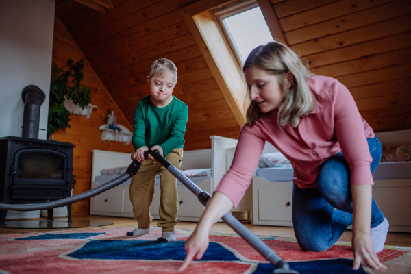 A boy with Down syndrome with his mother vacuum cleaning at home