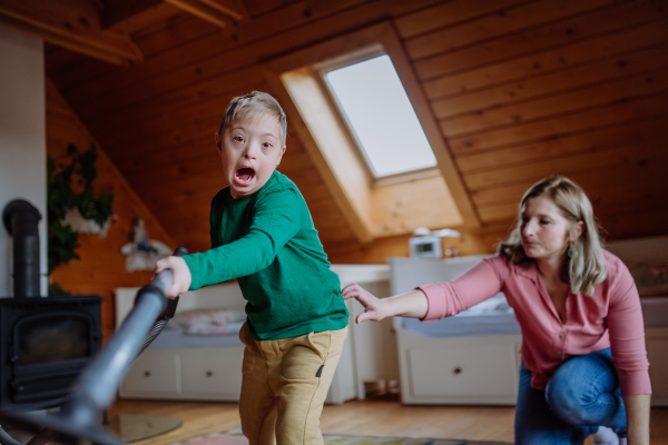 A boy with Down syndrome with his mother vacuum cleaning at home