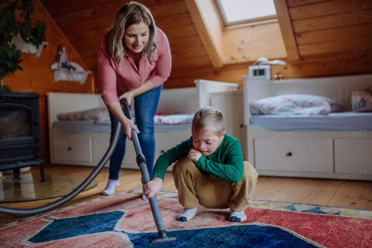 A boy with Down syndrome with his mother vacuum cleaning at home