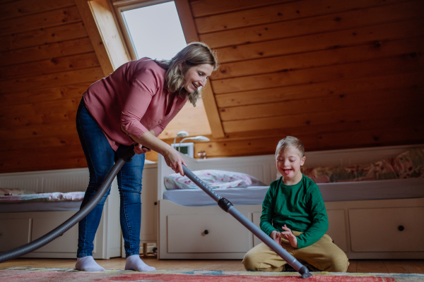 A boy with Down syndrome with his mother vacuum cleaning at home