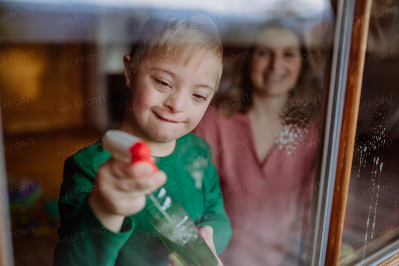 A boy with Down syndrome with his mother cleaning window at home.