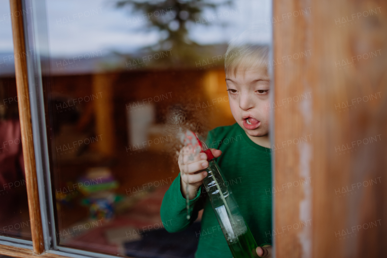 A boy with Down syndrome cleaning window at home.