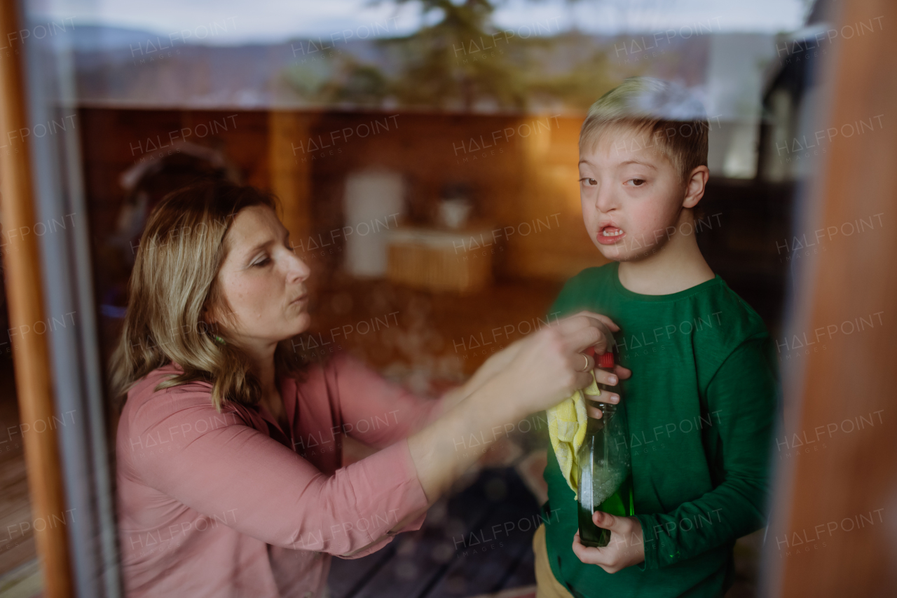 A boy with Down syndrome with his mother cleaning window at home.