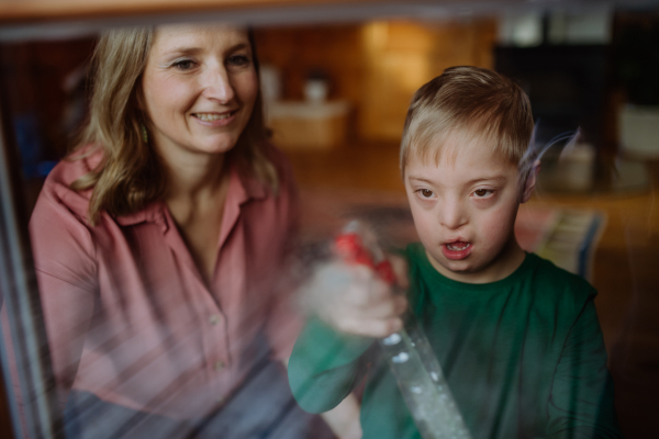 A boy with Down syndrome with his mother cleaning window at home.