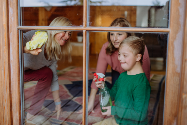 A boy with Down syndrome with his mother and grandmother cleaning window at home.