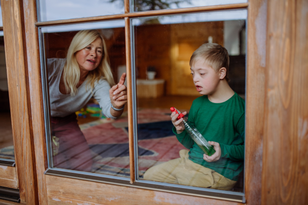 A boy with Down syndrome with his mother and grandmother cleaning window at home.