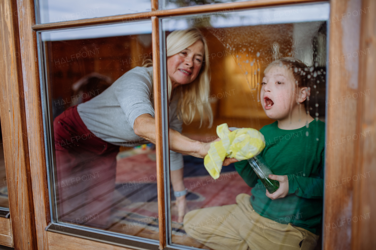 A boy with Down syndrome with his mother and grandmother cleaning window at home.