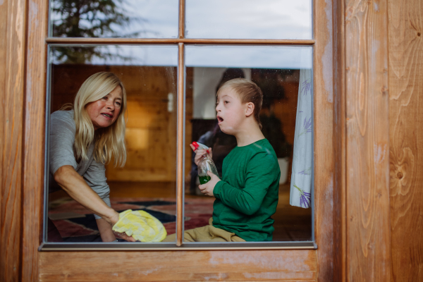 A boy with Down syndrome with his mother and grandmother cleaning window at home.