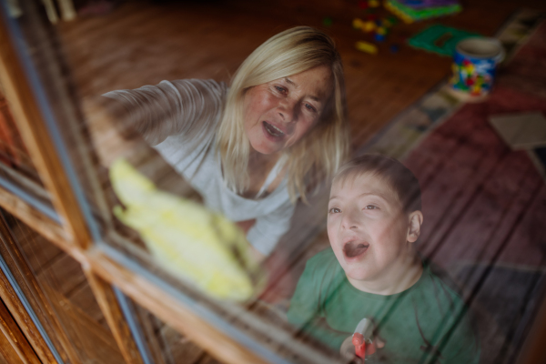 A boy with Down syndrome with his mother and grandmother cleaning window at home.