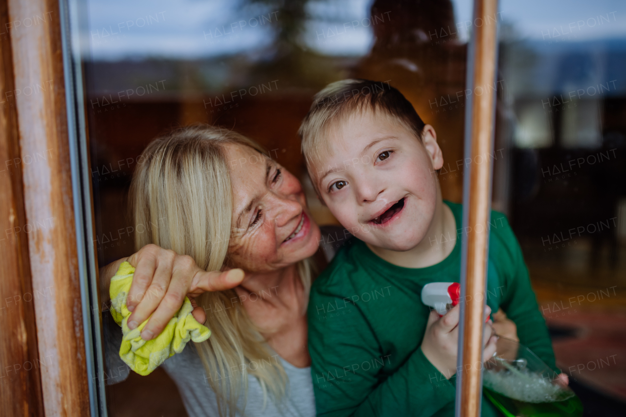 A boy with Down syndrome with his mother and grandmother cleaning window at home.