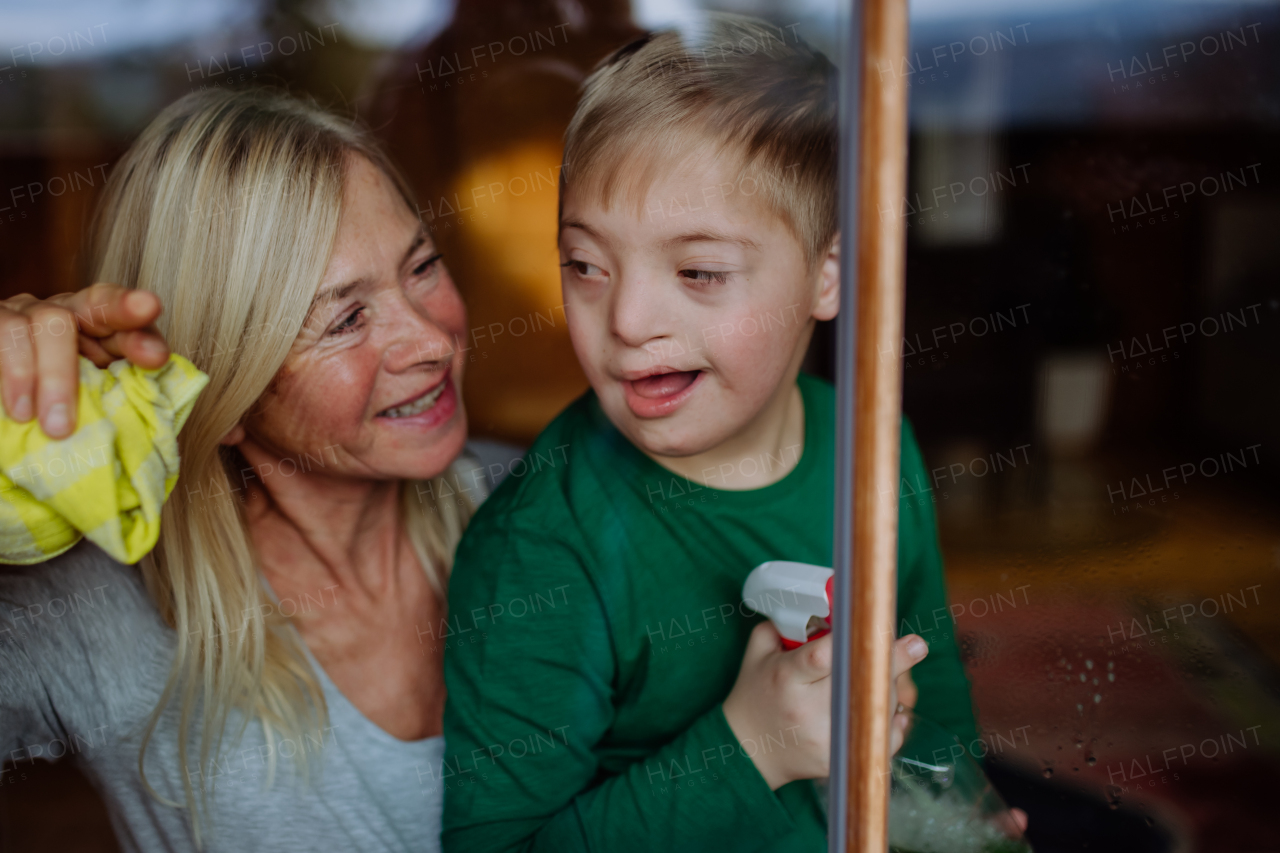 A boy with Down syndrome with his grandmother cleaning window at home.