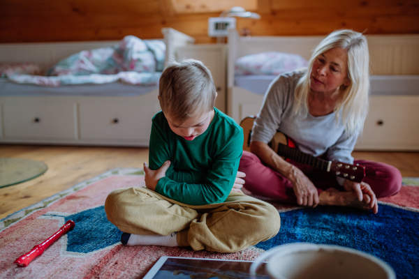 A boy with Down syndrome sitting on floor and playing with his grandmother at home