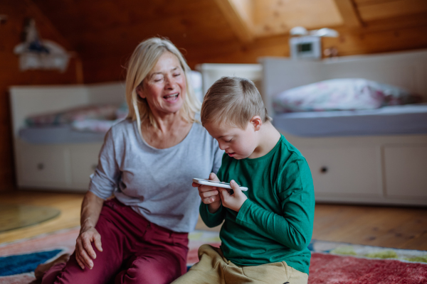 A child with Down syndrome sitting on floor and using tablet with grandmother at home.