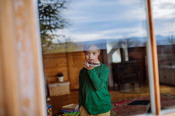 A sad little boy with Down syndrome using smartphone at home