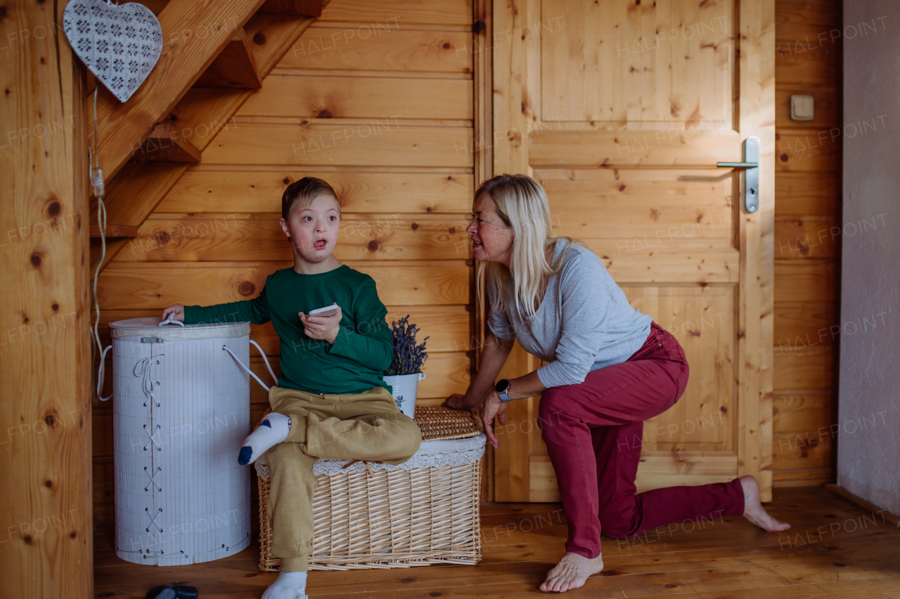 A child with Down syndrome sitting on floor and using tablet with grandmother at home.