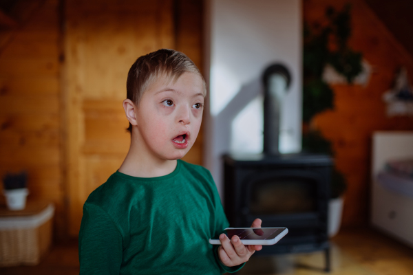 A little boy with Down syndrome sitting on floor and using smartphone at home.