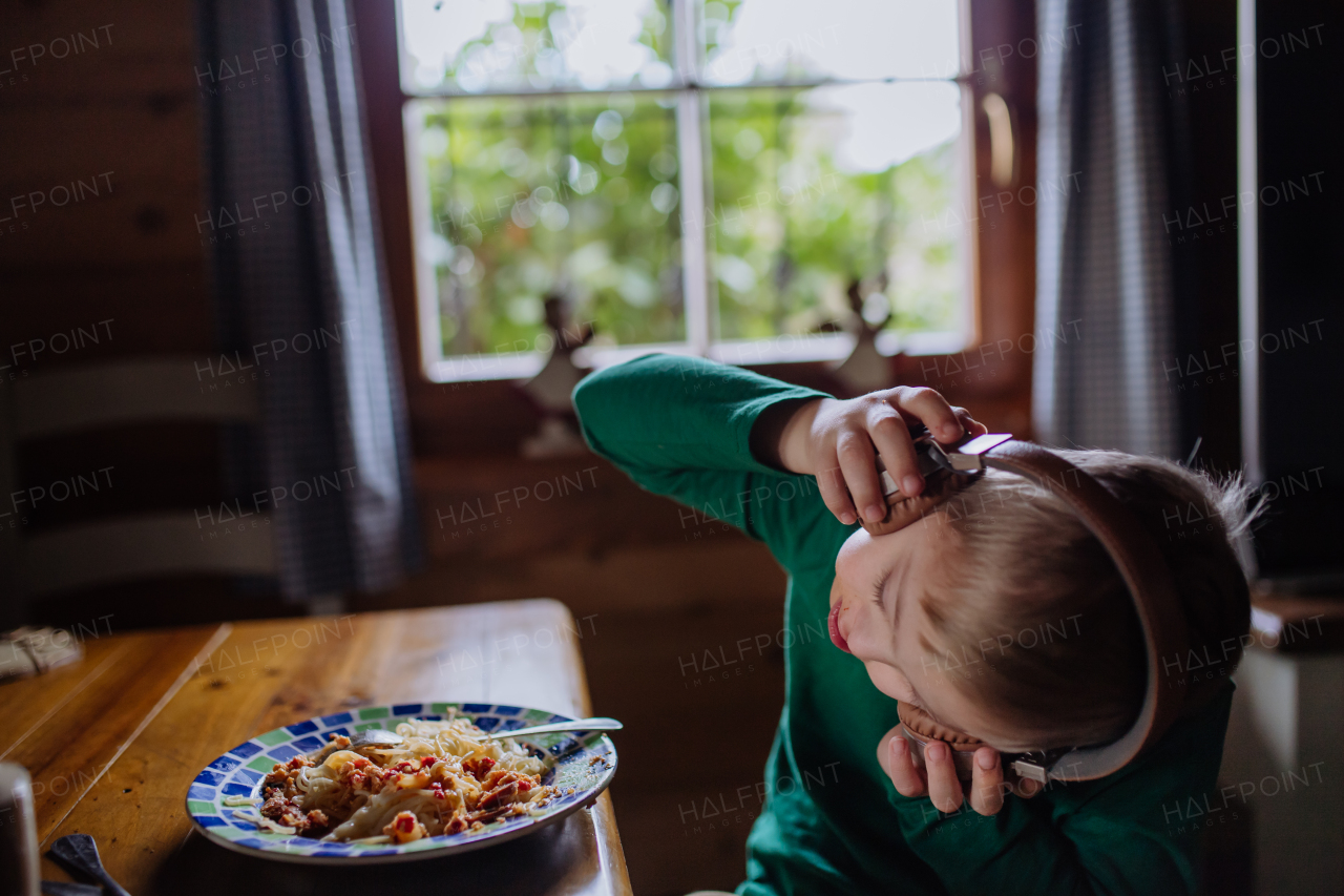 A boy with Down syndrome having lunch with headphones and looking at camera at home.