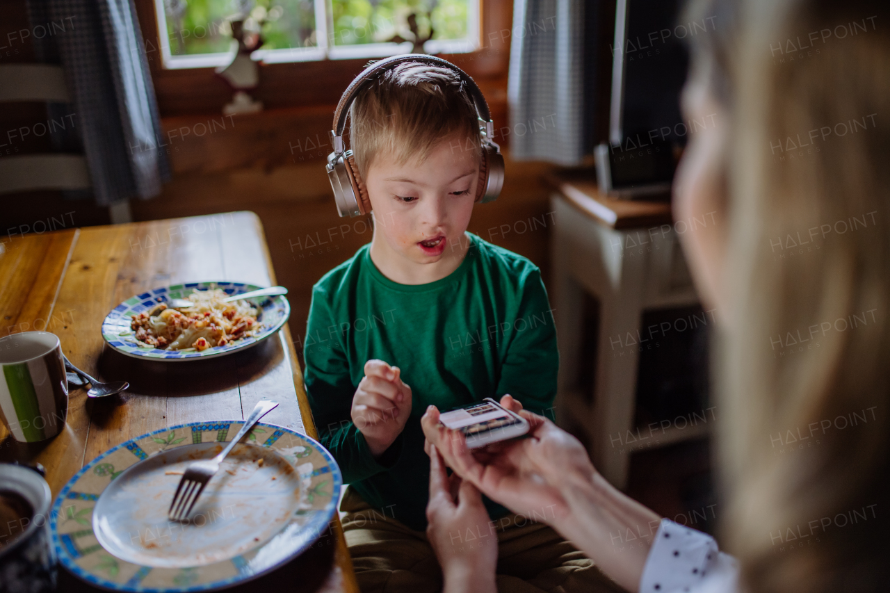 A boy with Down syndrome with his mother having lunch and using smartphone at home